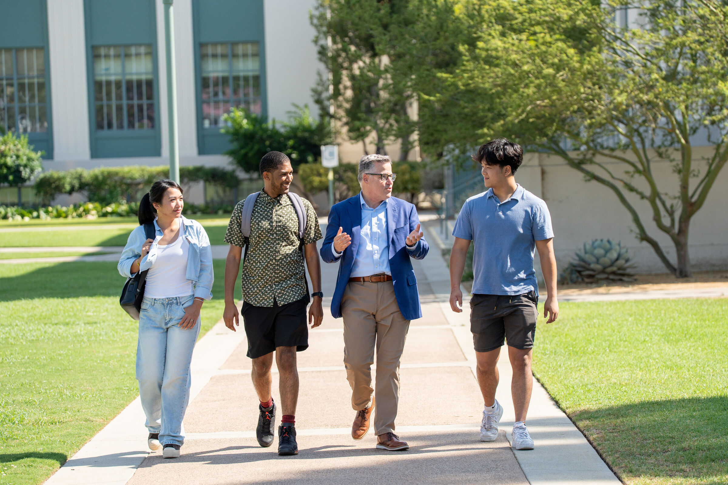 Geoff Baum walking and talking with four Pasadena City College students on a sunlit campus walkway.