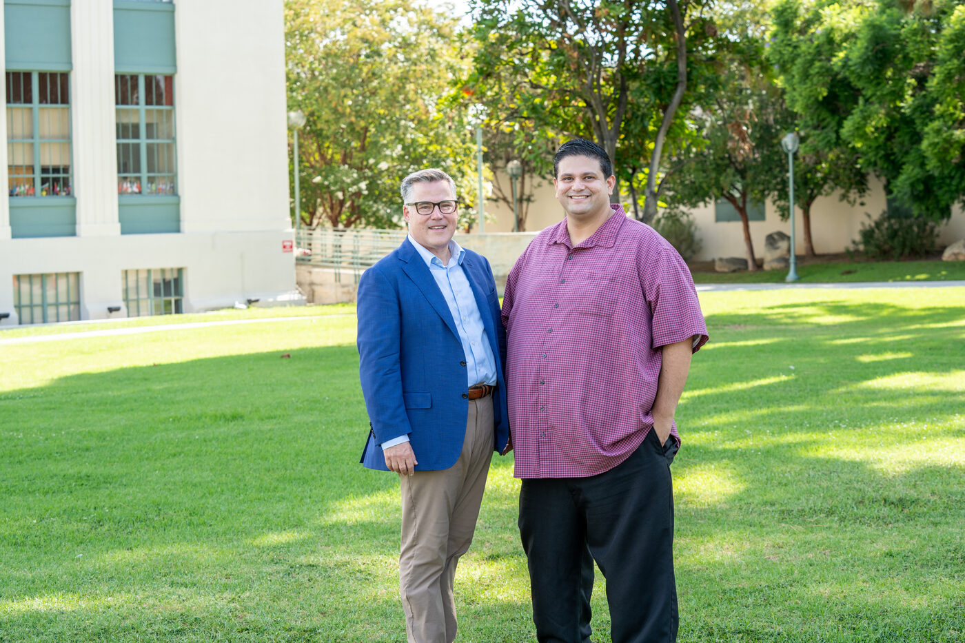 Geoff Baum standing and smiling beside another man on a campus lawn.